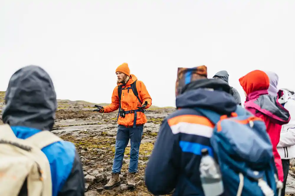 A guide in an orange jacket talking to the group out on the lava