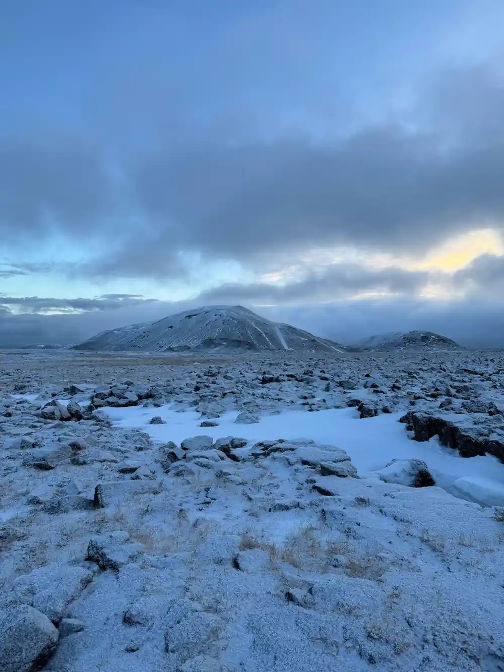 The lava field under snow at dusk with a cone on the horizon