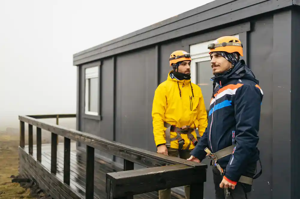 Two guides in helmets and harnesses outside the mountain cabin